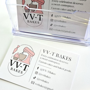 K&ouml;nnte beinhalten: Eine wei&szlig;e Visitenkarte f&uuml;r VV-T Bakes mit einem rosa Standmixer- und Cupcake-Logo, dem Text "Every celebration deserves a sweet centrepiece. Custom cakes and baked goods" sowie Social-Media-Kontaktdaten f&uuml;r Facebook, Instagram, TikTok und E-Mail.