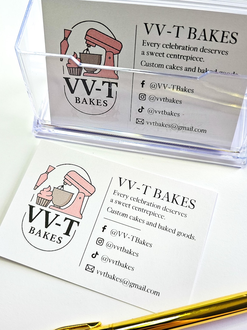 K&ouml;nnte beinhalten: Eine wei&szlig;e Visitenkarte f&uuml;r VV-T Bakes mit einem rosa Standmixer- und Cupcake-Logo, dem Text "Every celebration deserves a sweet centrepiece. Custom cakes and baked goods" sowie Social-Media-Kontaktdaten f&uuml;r Facebook, Instagram, TikTok und E-Mail.