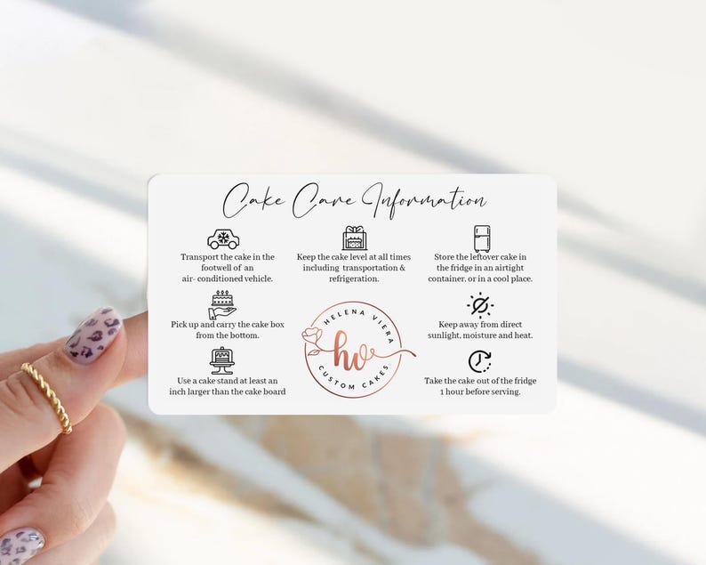 Peut inclure: Une carte rectangulaire blanche intitul&eacute;e Cake Care Information avec du texte et des ic&ocirc;nes noirs. Elle fournit des instructions pour le transport, le stockage et le service des g&acirc;teaux, avec un logo central Helena Viera Custom Cakes.