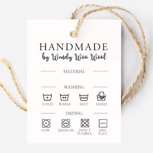 May include: A rectangular white paper tag with a jute twine string. The text reads HANDMADE by Wendy Woo Wool, MATERIAL, WASHING, COLD, WARM, HOT, HAND, DRYING, LOW, MEDIUM, DON'T TUMBLE, and DRY FLAT, accompanied by various laundry care icons.