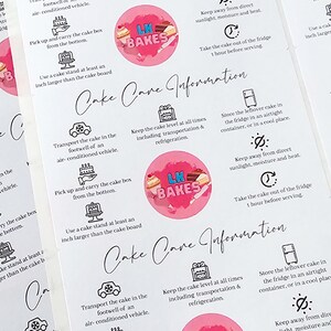 Peut inclure: Une feuille d'autocollants rectangulaires blancs avec le texte Cake Care Information et des ic&ocirc;nes en ligne noire. Chaque autocollant contient des instructions pour le transport et le stockage des g&acirc;teaux, avec un logo circulaire rose LK BAKES.