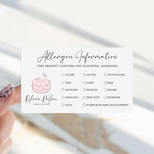 May include: A rectangular white allergen information card featuring the text Allergen Information and This product contains the following allergens. It includes a pink line-art cake illustration, the Olivia Wilson Cake & Dessert logo, and a checklist of allergens including celery, gluten, crustaceans, fish, lupin, milk, mustard, peanuts, sesame, molluscs, tree nuts, soybeans, eggs, and sulphur dioxide and sulphites.