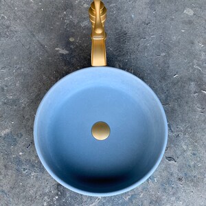 May include: A round, light blue ceramic sink with a gold faucet and drain.