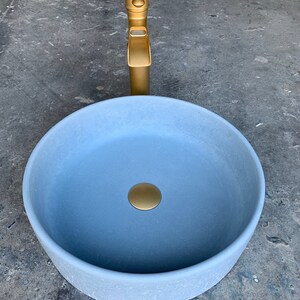 May include: A light blue ceramic bathroom sink with a gold drain stopper and a gold faucet.