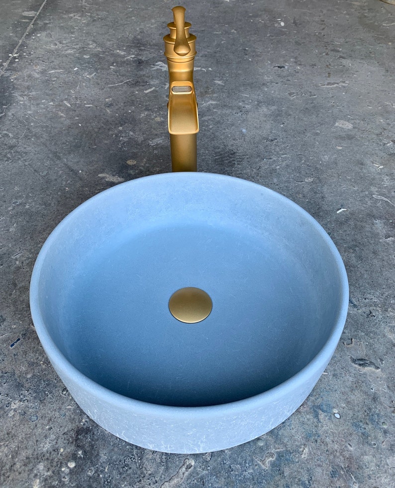 May include: A light blue ceramic bathroom sink with a gold drain stopper and a gold faucet.