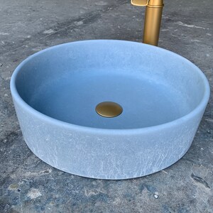 May include: A light blue round ceramic sink with a gold drain stopper. The sink has a textured surface and is designed for a bathroom.