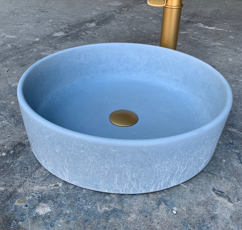 May include: A light blue round ceramic sink with a gold drain stopper. The sink has a textured surface and is designed for a bathroom.