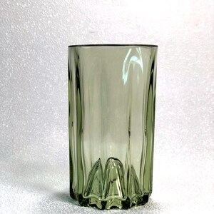 May include: A tall, olive-green glass with vertical ridges and a decorative base. The glass has a simple, yet elegant design, suitable for serving beverages. The glass is approximately 6 inches tall.