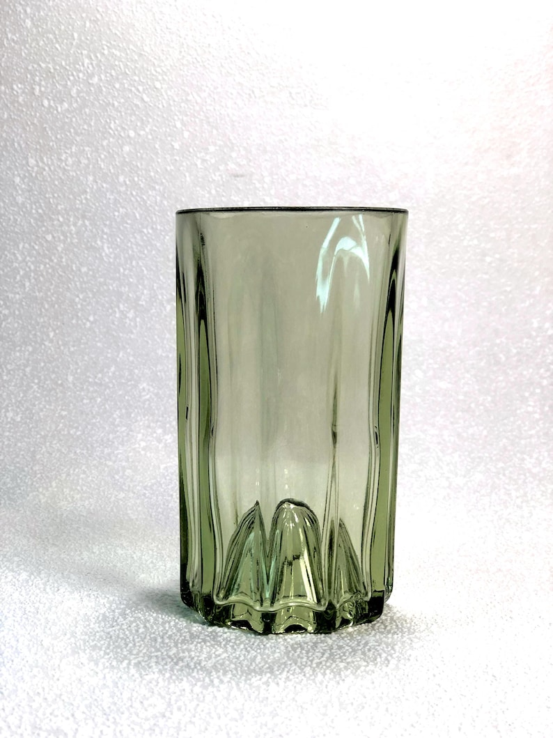 May include: A tall, olive-green glass with vertical ridges and a decorative base. The glass has a simple, yet elegant design, suitable for serving beverages. The glass is approximately 6 inches tall.