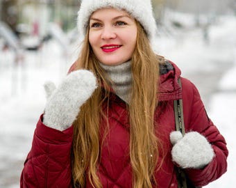 Puede incluir: Una mujer con un gorro de punto blanco, una chaqueta acolchada roja y guantes de punto blancos. Está de pie en un entorno nevado.