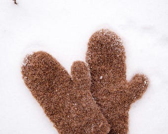 Puede incluir: Un par de guantes de lana marrón peludos sobre una superficie nevada.
