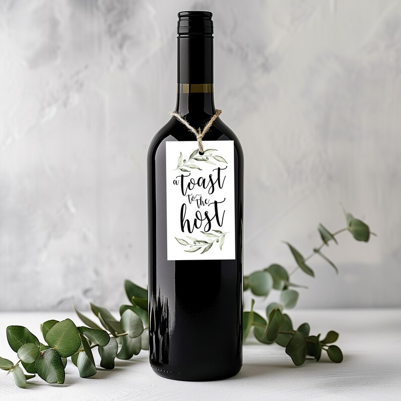May include: A dark glass wine bottle with a rectangular white paper tag tied around the neck with twine. The tag features green watercolour olive branch illustrations and the black printed text A toast to the host in a decorative script font.