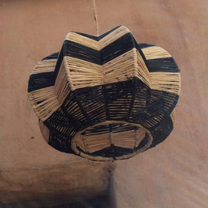 May include: A black and natural woven pendant light fixture with a geometric design. The light fixture is made of natural materials and has a rustic look.