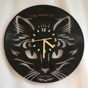 May include: Black vinyl record clock featuring a white silhouette of a cat's face. The clock face is black with white numbers and gold hands.