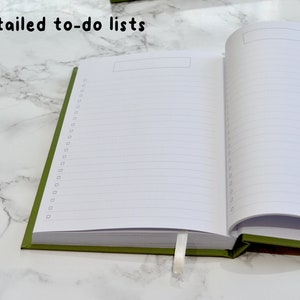 May include: An open green journal with the words "Detailed to-do lists" printed on the cover. The journal has lined pages and a blank space at the top of each page.
