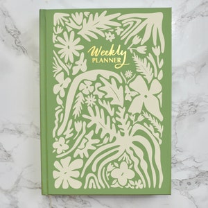 May include: A green weekly planner with a white floral design and the text "Weekly Planner" in gold lettering.