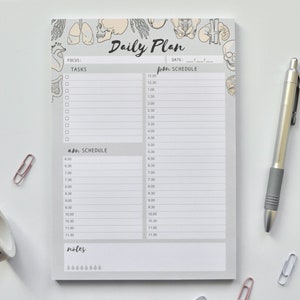 Könnte beinhalten: Ein grau-weißer Tagesplaner mit medizinischem Illustrationsthema. Der Planer hat einen Bereich für Aufgaben, einen Zeitplan für den Vormittag und Nachmittag sowie einen Notizbereich. Der Planer enthält einen Schädel, ein Herz, Lungen und andere anatomische Illustrationen.