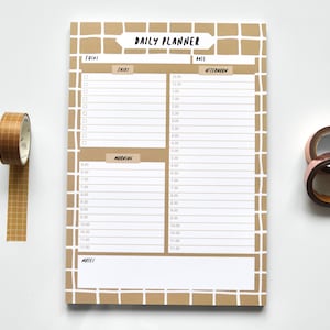 May include: A brown daily planner with a grid pattern and the words "DAILY PLANNER" at the top. The planner has sections for "Focus", "Tasks", "Morning", "Afternoon", and "Notes".