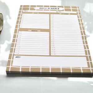 May include: A brown daily planner with a grid pattern and white lines. The planner has a section for "Morning" and "Afternoon" with time slots from 8:00 AM to 11:30 AM. The planner also has a section for "Notes".