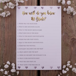 May include: A printable bridal shower game with the title "How well do you know the Bride?" and 14 questions about the bride. The game is printed on white paper with a light purple background and has a decorative border of hearts.