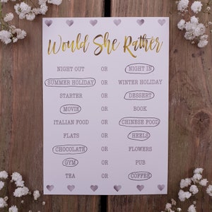 May include: A printable "Would She Rather" game card with a light purple background and gold text. The card features a series of questions with two choices for each question, such as "Night Out" or "Night In", "Summer Holiday" or "Winter Holiday", and "Chocolate" or "Flowers".