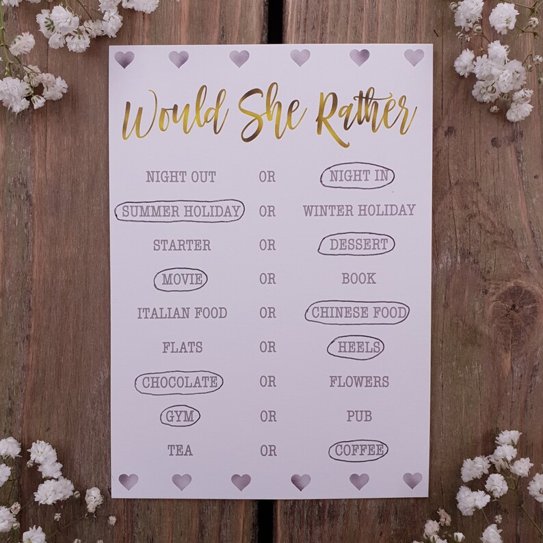May include: A printable "Would She Rather" game card with a light purple background and gold text. The card features a series of questions with two choices for each question, such as "Night Out" or "Night In", "Summer Holiday" or "Winter Holiday", and "Chocolate" or "Flowers".
