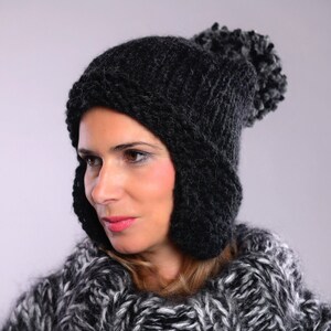 May include: A black knit hat with ear flaps and a pom-pom on top. The hat is made of a thick, warm yarn and has a cozy, wintery feel.