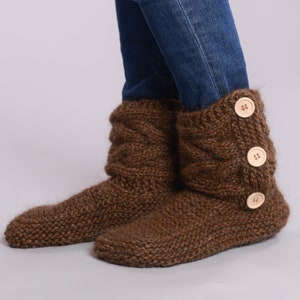 May include: Brown knitted slipper boots with wooden buttons. The boots are folded down at the top and have a cable knit pattern.