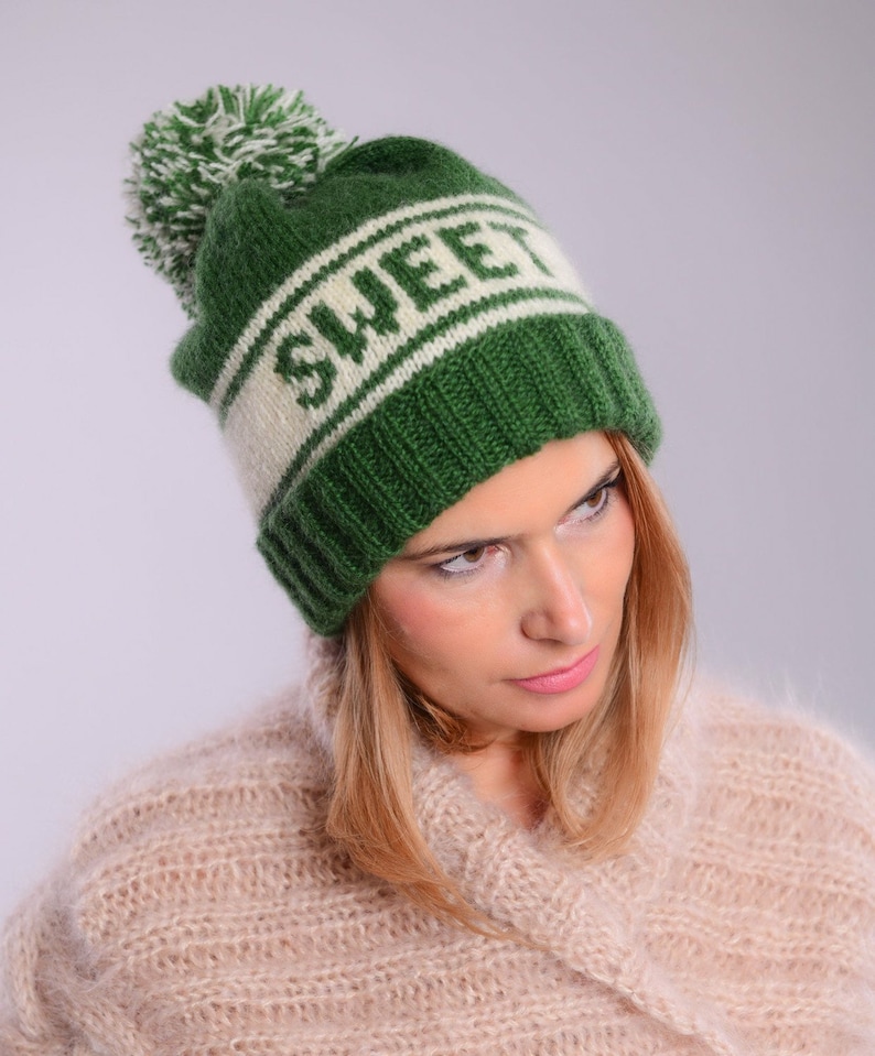 May include: Green knitted beanie with a white pom pom and the word "SWEET" in white lettering on a white stripe.
