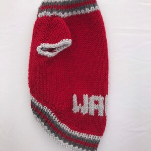 Pu&ograve; includere: Maglia di lana rossa per cani con bordini grigi e la parola "WARRIOR" lavorata a maglia in grigio sul davanti.
