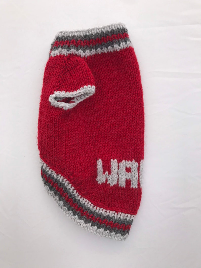 Pu&ograve; includere: Maglia di lana rossa per cani con bordini grigi e la parola "WARRIOR" lavorata a maglia in grigio sul davanti.