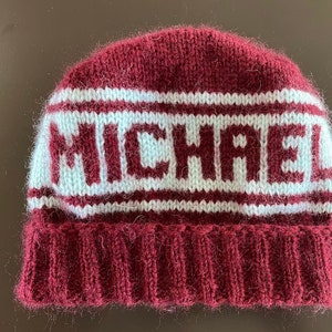 May include: A maroon knitted beanie with white stripes and the word "MICHAEL" knitted in white.