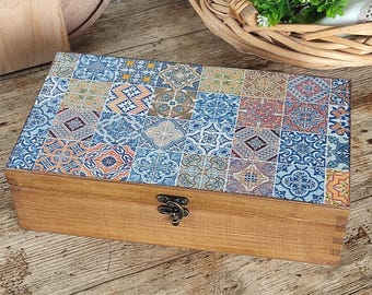May include: A rectangular wooden storage box featuring a hinged lid decorated with a colorful mosaic pattern of various blue, orange, and yellow geometric tile designs. The box has a natural wood grain finish and a small, dark metal latch on the front.