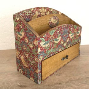 Op de afbeelding: Houten bureau-organizer met een lade en meerdere compartimenten. De organizer is bedekt met een rood, groen en beige bloemen- en vogelpatroon. De lade heeft een kleine metalen handgreep.