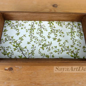 May include: A rectangular wooden serving tray with cutout handles on both sides. The interior base features a light-colored surface decorated with a repeating pattern of green leaves and thin brown branches. The text SayaArtDesign is visible.