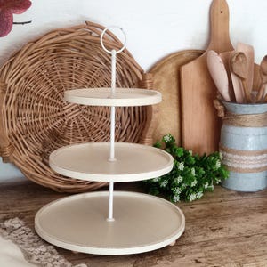 May include: A three-tiered white serving stand with a metal frame. The stand has a distressed white finish and is perfect for displaying desserts, snacks, or other treats.
