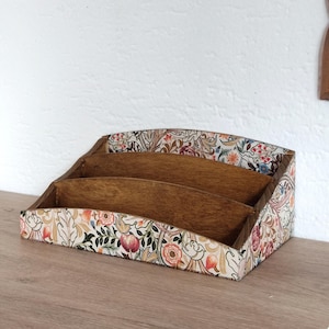 Op de afbeelding: Een houten bureau-organizer met drie vakken, versierd met een bloemenpatroon in tinten roze, rood, groen en blauw.