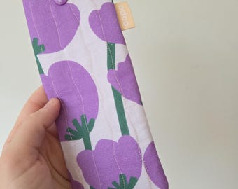 May include: A rectangular glasses case with a floral pattern of purple tulips on a white background. The case has a button closure and a small, rectangular tag with the word "odoo" on it. The case is held in a hand.