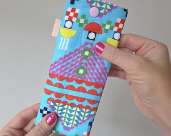 May include: A colorful fabric glasses case with a geometric pattern in shades of blue, pink, red, yellow, and white. The case has a snap closure and a small label with the word "dodo".