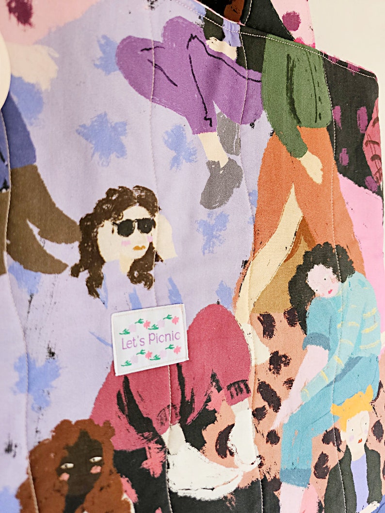 Pu&ograve; includere: Una borsa tote trapuntata con una stampa colorata di figure in varie pose. Il design include sfumature di viola, rosa, marrone e blu, con un'etichetta che recita "Let's Picnic". La borsa presenta un motivo cucito.