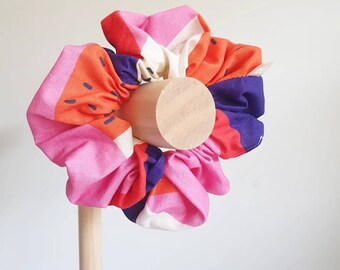 Può includere: Un assortimento di elastici per capelli colorati in rosa, arancione, viola e bianco, esposti su un supporto di legno. Gli elastici presentano un motivo geometrico audace con dettagli neri, perfetti per aggiungere colore a qualsiasi acconciatura.