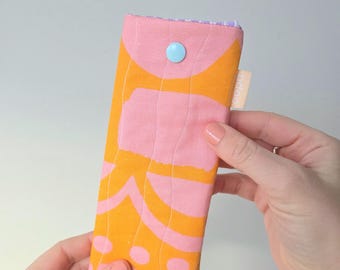 May include: A rectangular fabric pouch featuring a bold orange and pink abstract pattern with wavy quilted stitching. The case is secured with a single light blue plastic snap button and includes a small beige fabric tag with the text odoo.