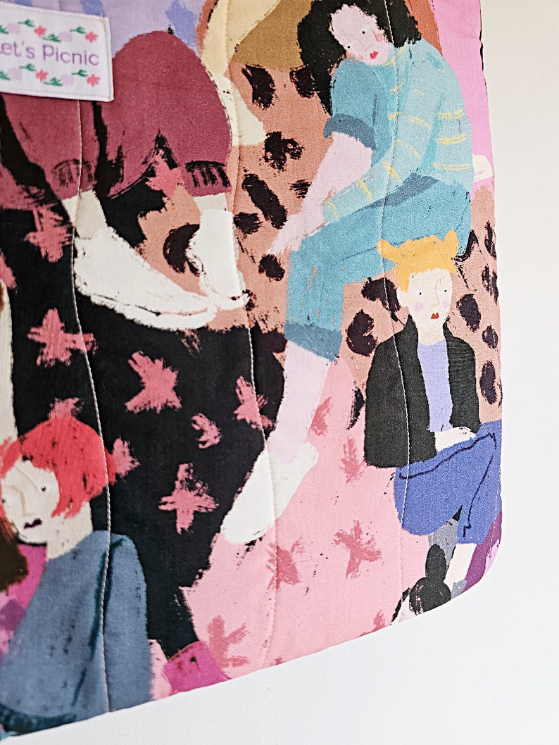 Pu&ograve; includere: Borsa tote trapuntata con un colorato design astratto con figure in varie pose. La borsa ha una combinazione di colori rosa, nero e marrone con un'etichetta che recita "Let's Picnic". Il design include forme di stelle rosa.