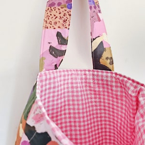 Pu&ograve; includere: Una borsa tote con esterno rosa fantasia e interno a quadretti rosa. L'esterno presenta un collage di forme astratte in rosa, viola, nero e beige. I manici sono rosa e fantasia, in linea con il design esterno.