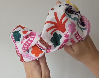 May include: A white fabric headband with a colorful pattern of abstract shapes in red, pink, green, and brown. The headband is held in two hands.