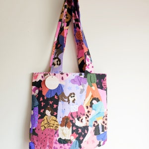 Pu&ograve; includere: Una borsa tote trapuntata con un motivo colorato di figure in varie pose. La borsa presenta un mix di tonalit&agrave; rosa, viola, nere e gialle. I manici e il corpo della borsa sono realizzati con lo stesso tessuto fantasia. &Egrave; attaccato un piccolo tag rotondo con la scritta "oops".