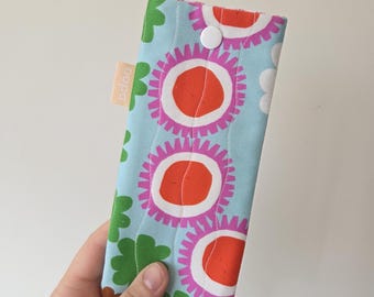 May include: A light blue fabric case with a floral pattern featuring large orange and pink flowers. The case has a white button closure and a small rectangular tag with the word "odoo".