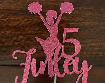 Puede incluir: Topper de pastel de purpurina rosa con una silueta de animadora sosteniendo pompones, el número 5 y el nombre Finley.