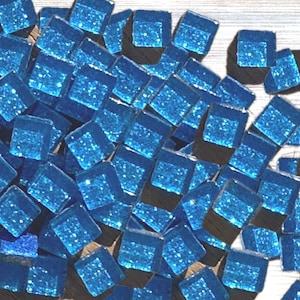 May include: A collection of small, square, crystal glass mosaic tiles in shades of blue. The image includes the text "Crystal Glass Mosaic Tiles (approx. 200)". The tiles are scattered on a light-colored wooden surface.