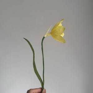 May include: A single yellow paper flower with green paper stems.